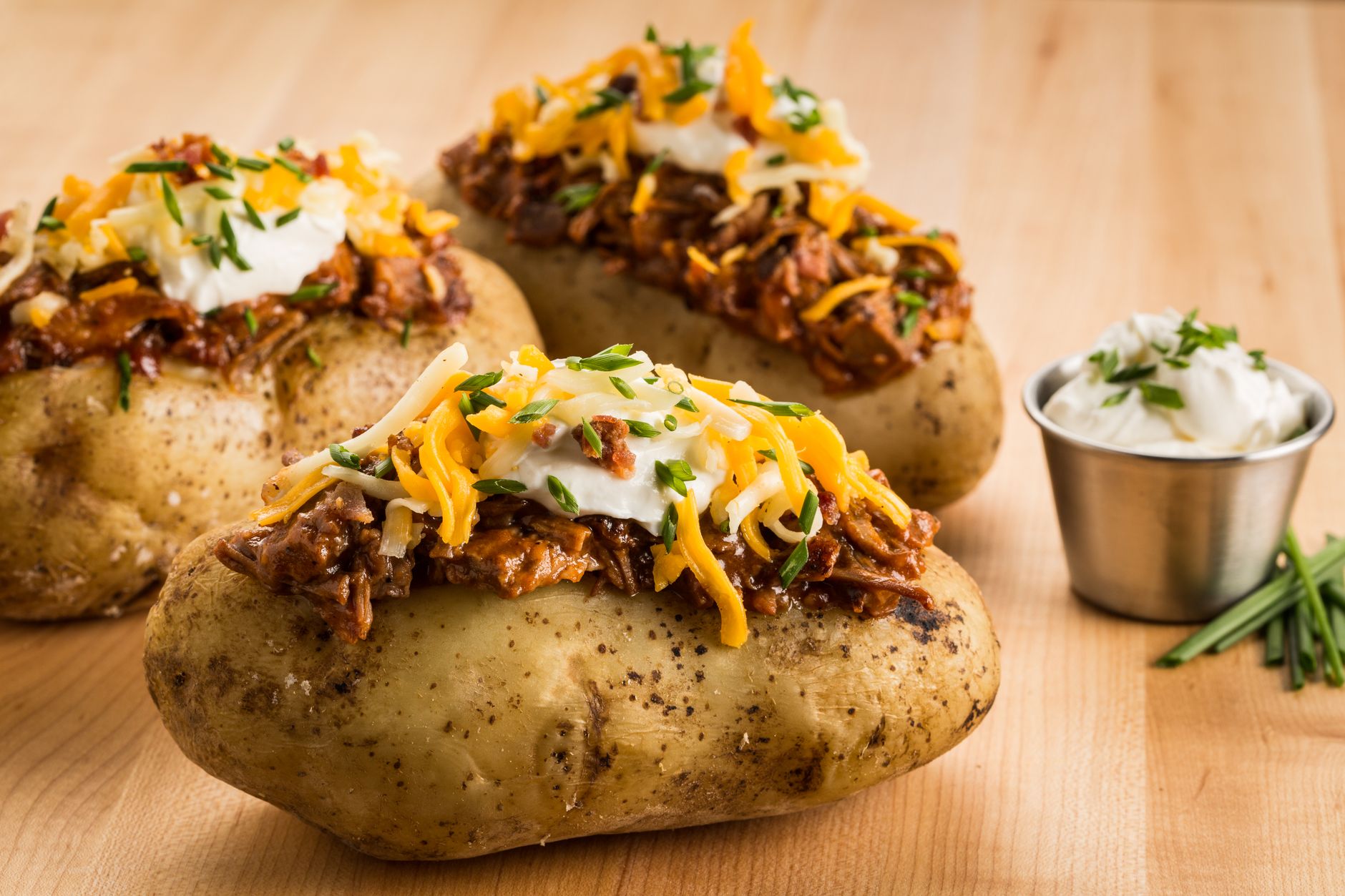 Air fryer baked potato for one topped with cheese, sour cream, and chives on a wooden board.