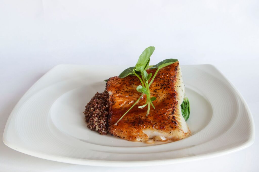 Cooked white fish fillet served with quinoa and greens on a white plate.
