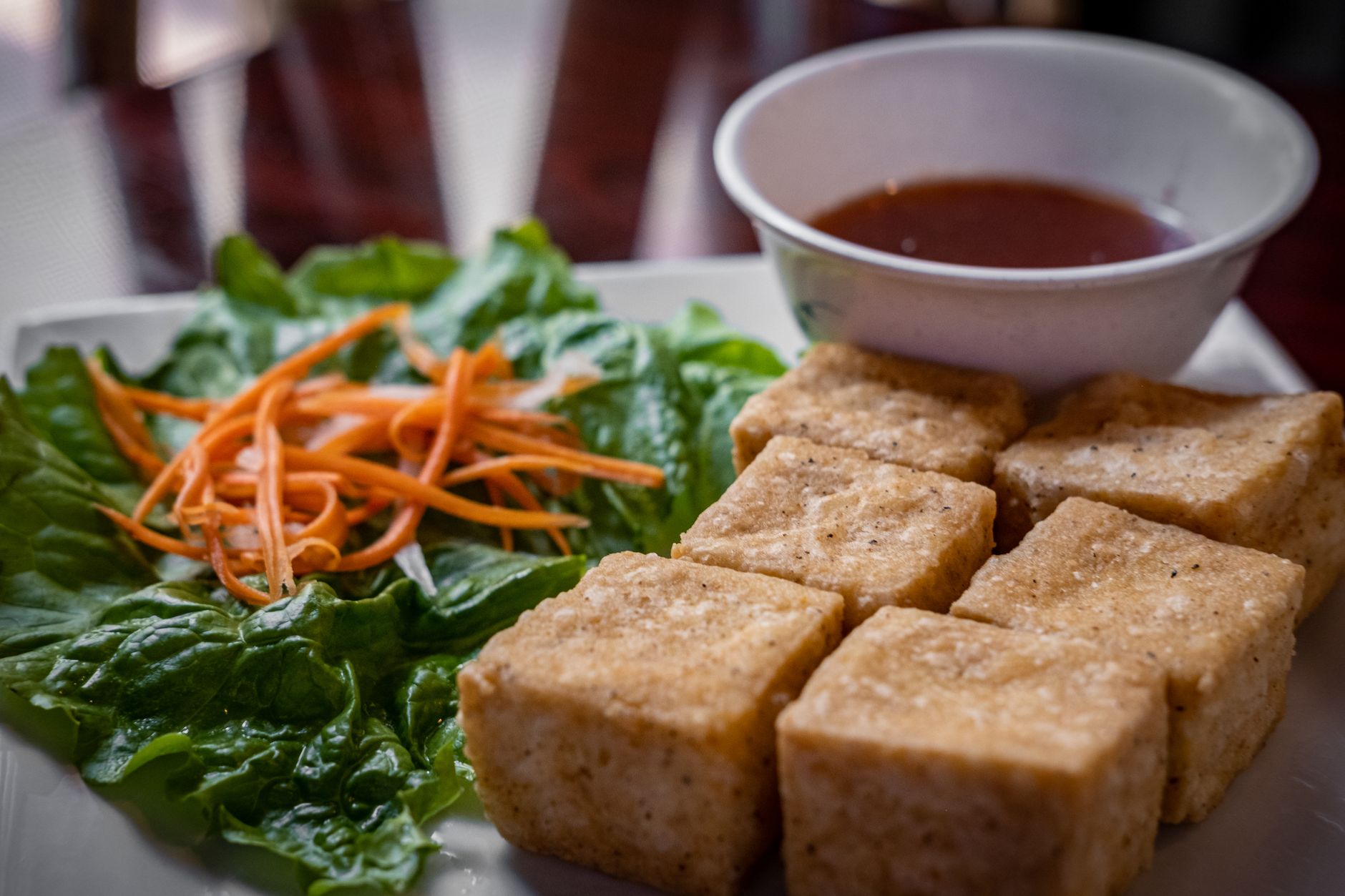 Air fryer tofu for one with crisp tofu cubes, greens, and dipping sauce.