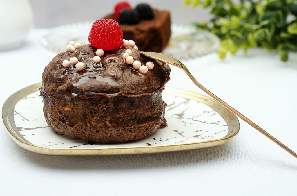Serving inspiration for air fryer chocolate cake for one: a small plated chocolate cake with raspberry and glaze, unlike the unfrosted ramekin recipe.