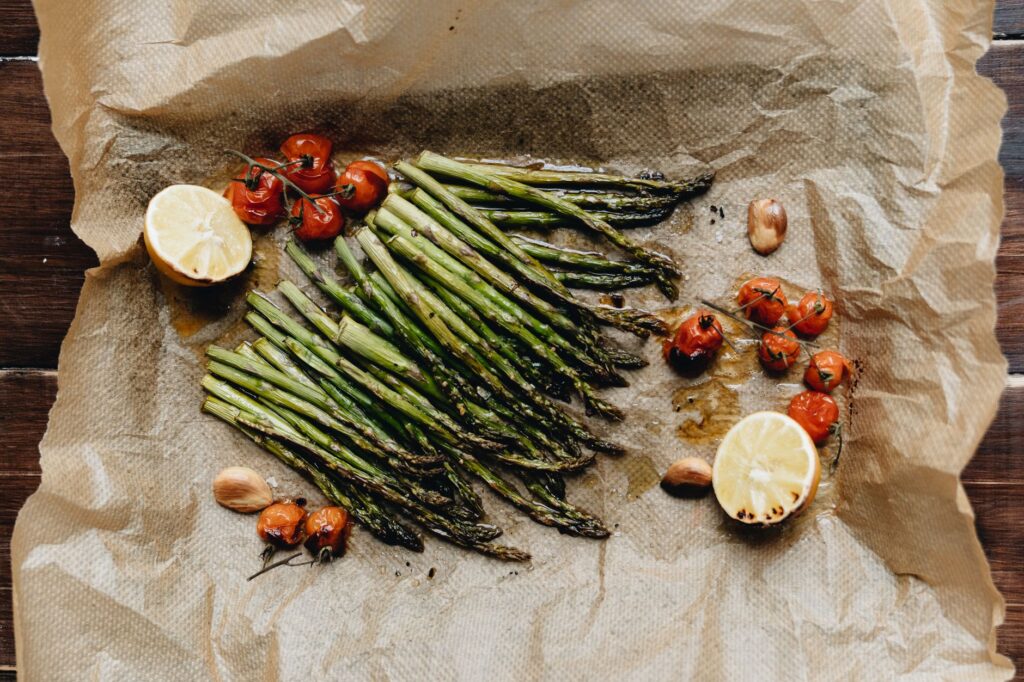 Air fryer asparagus for one serving inspiration: roasted asparagus spears with tomatoes and lemon on parchment.